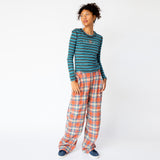 A model looks to the side while wearing the coral plaid wide leg Clover Pant by Collina Strada, paired with a blue striped long sleeve.