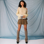 A model wears the pale yellow Composition sweater by Eckhaus Latta paired with a pleated mini skirt, leg warmers and black loafers, full outfit view.