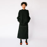 A model wears an oversized black sweater over the Misc Etc long Contrast Stitch Cargo Skirt in black - paired with black socks and red heels.