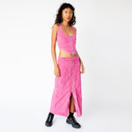 A model wears the pink corduroy Cord Bustier by Eckhaus Latta, with silver front zipper and wide shoulder straps, paired here with the matching full length corduroy zip skirt and black sneakers.