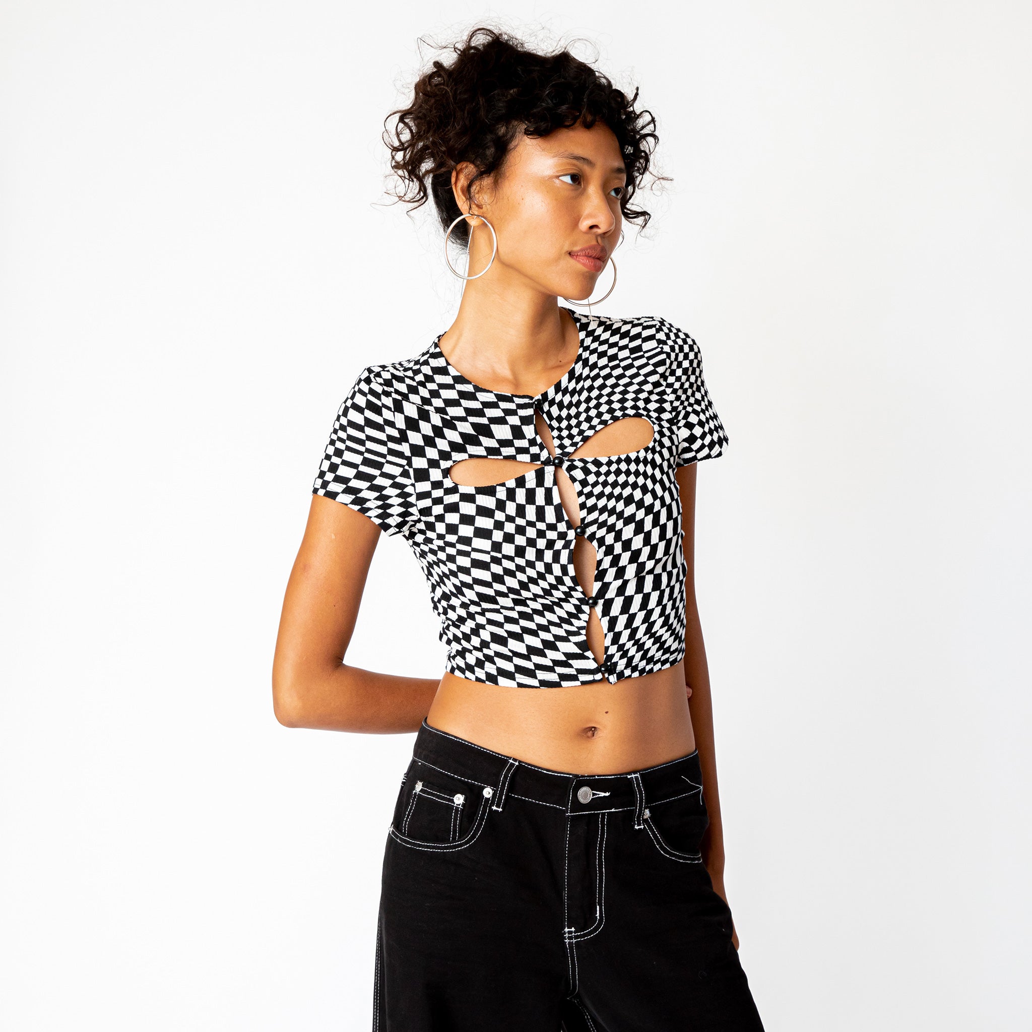 A model wears the black and white checkered cut out tee by Misc Etc, paired with black cargo pants while looking to the side.