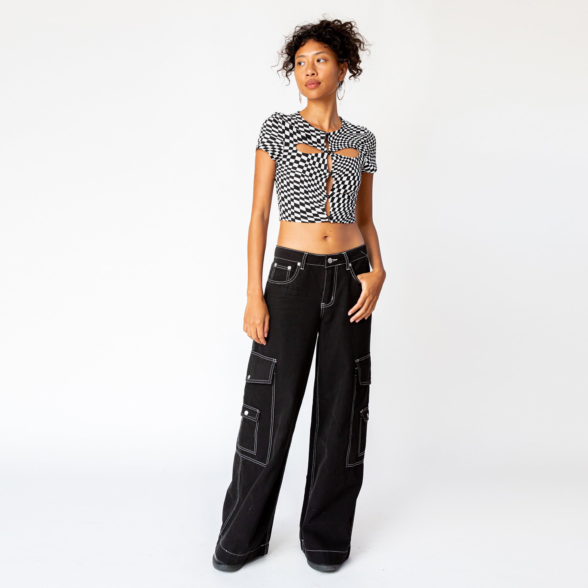 A model wears the black and white checkered cut out tee by Misc Etc, paired with black cargo pants - full outfit view.