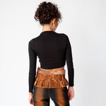 Back view of a model wearing the longsleeved black crop Mockneck top paired with brown and black gradient jeans and a velvet pleated belt.