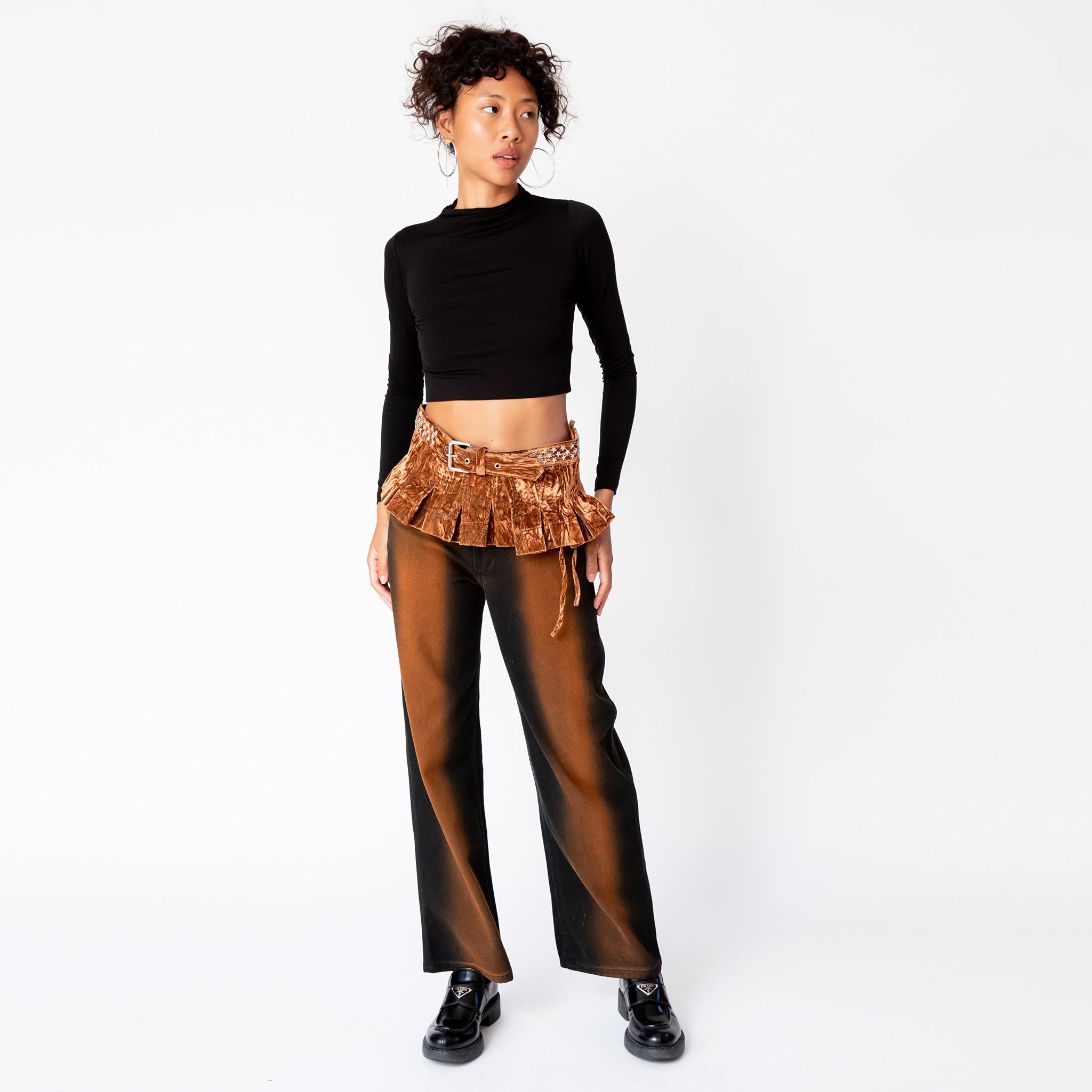 Full outfit view of a model wearing the longsleeved black crop Mockneck top paired with brown and black gradient jeans and a velvet pleated belt.