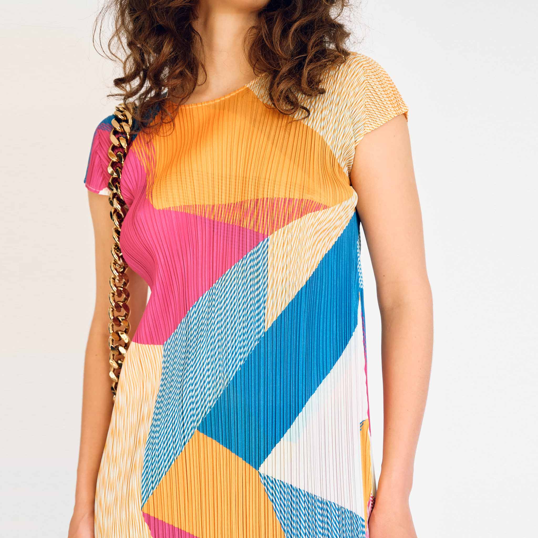 Graphic printed pleated short sleeve dress by Pleats Please, close up detail view on model.