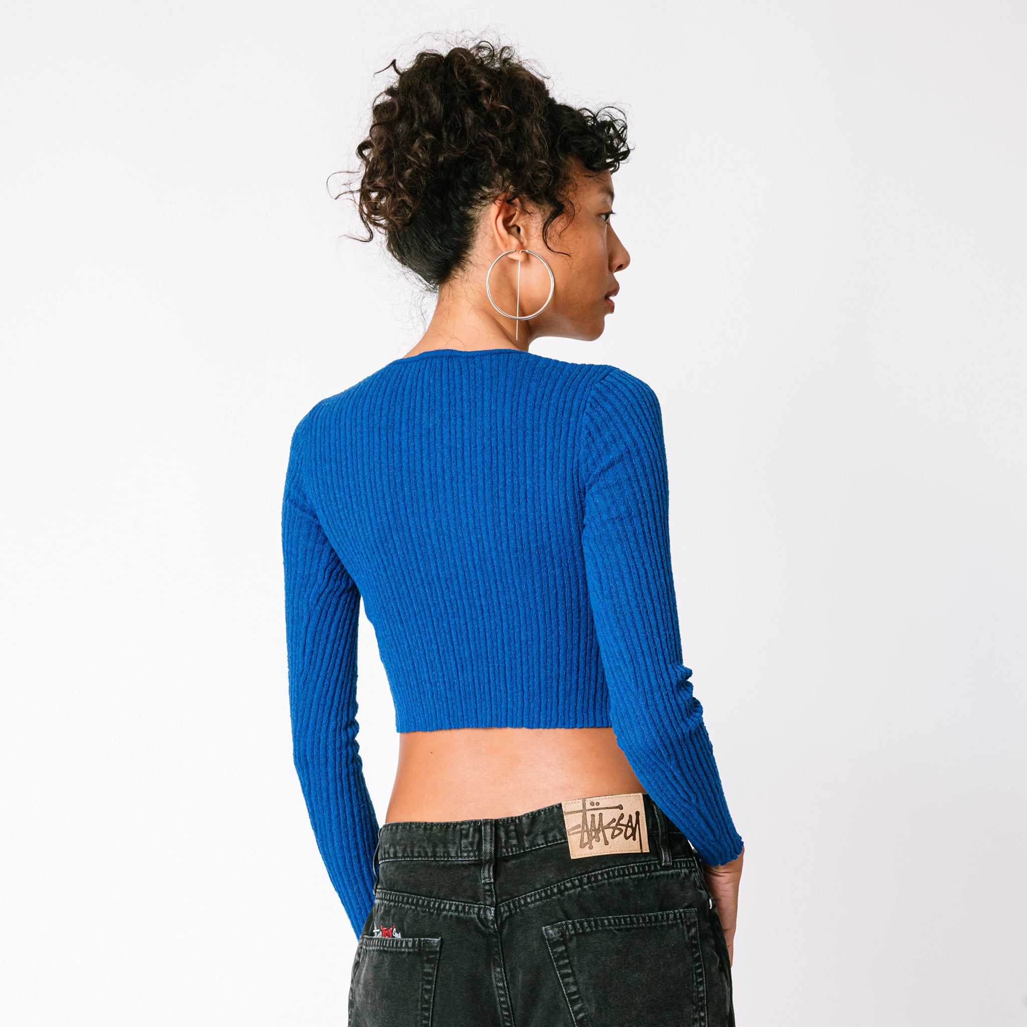 A model wears the electric blue cropped cardigan with multiple cutouts in a vertical line along the chest, back view.