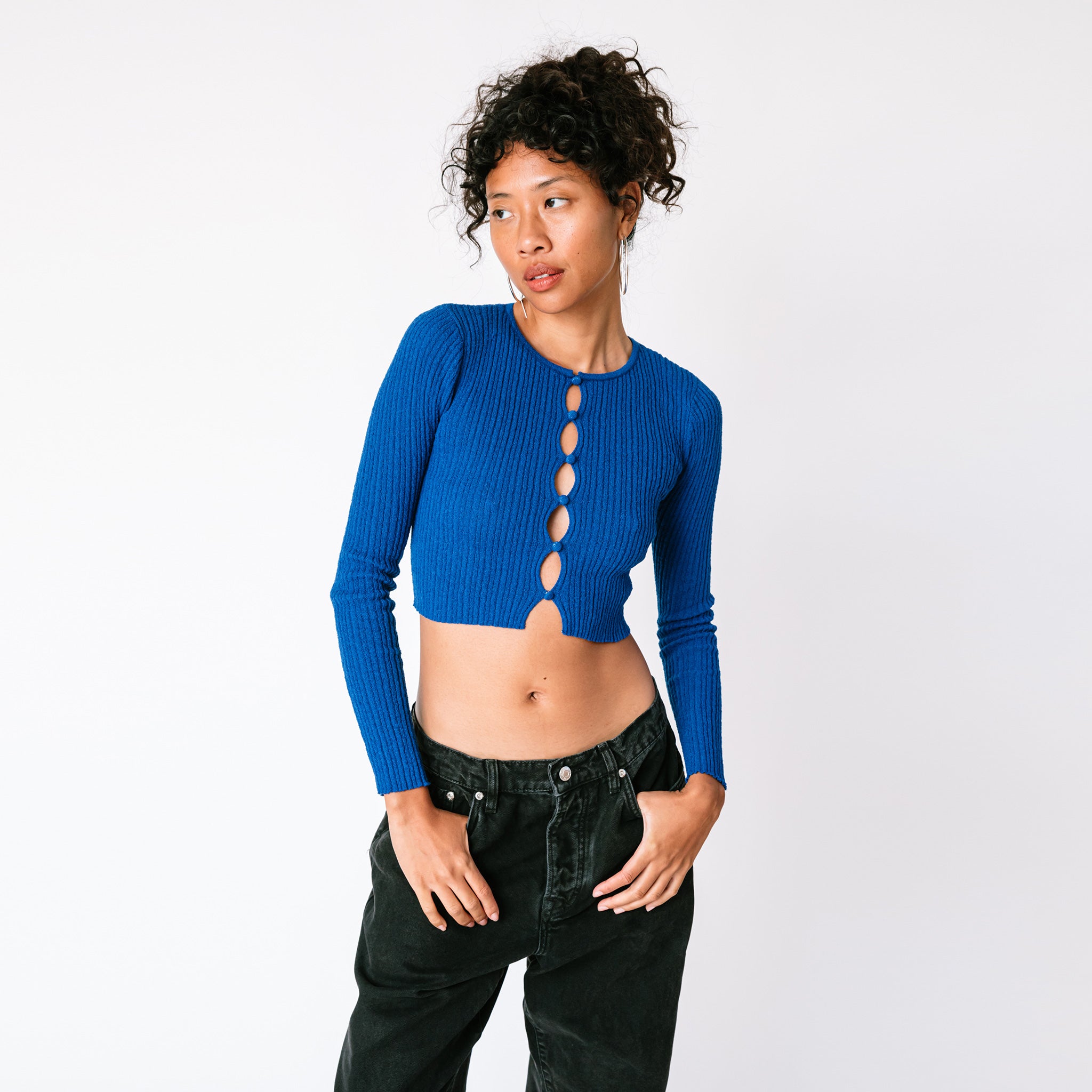 A model wears the electric blue cropped cardigan with multiple cutouts in a vertical line along the chest, paired with black jeans.