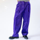 Front detailed photo of a model wearing the GANNI relaxed corduroy pants in purple, paired with a simple grey vest and black loafers.