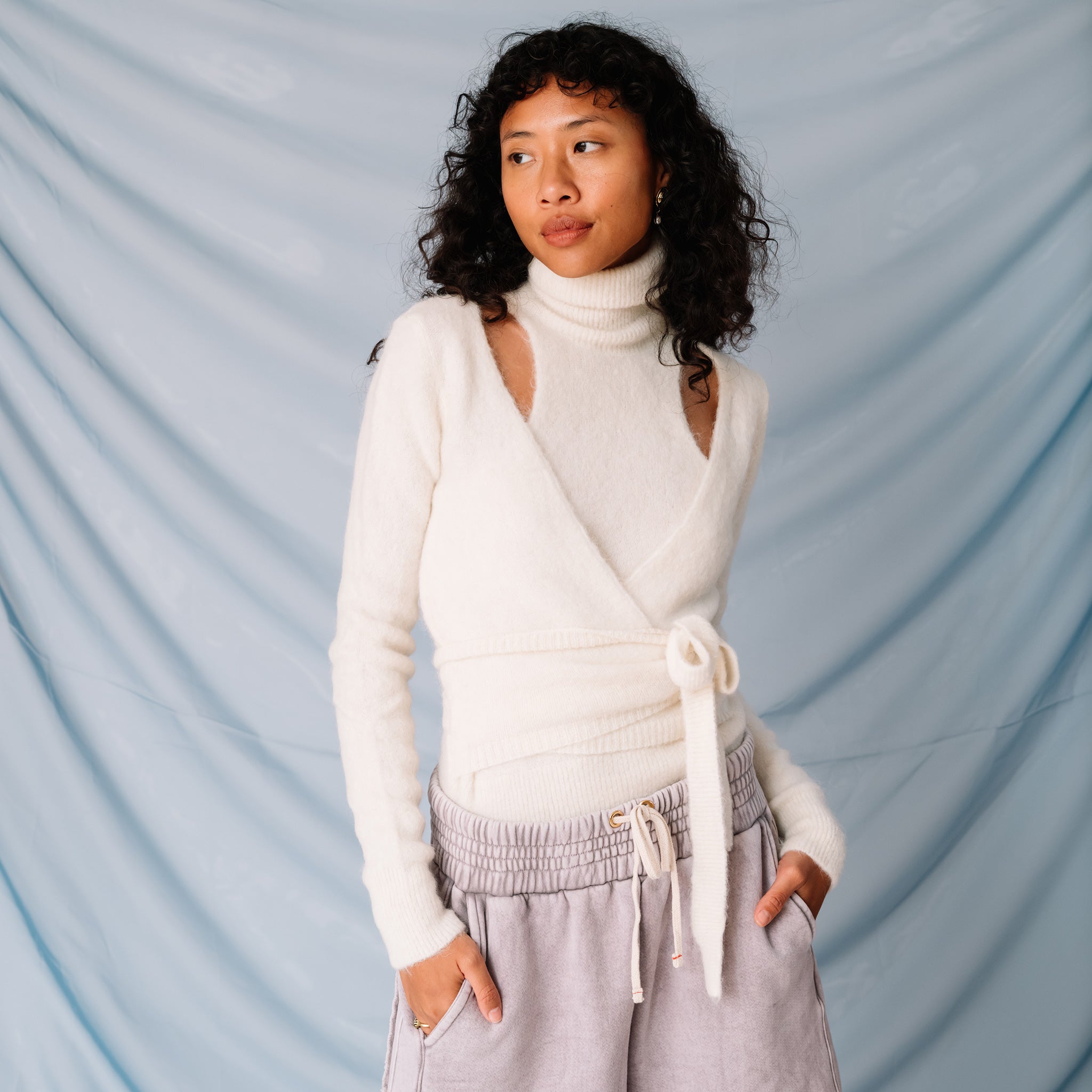 A model looks to the side while wearing a soft-looking white wrap sweater by GANNI with clavicle cut outs.