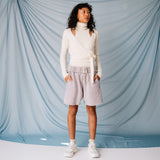A model looks to the side while wearing a soft-looking white wrap sweater by GANNI with clavicle cut outs, paired with pale lavender sweat shorts.