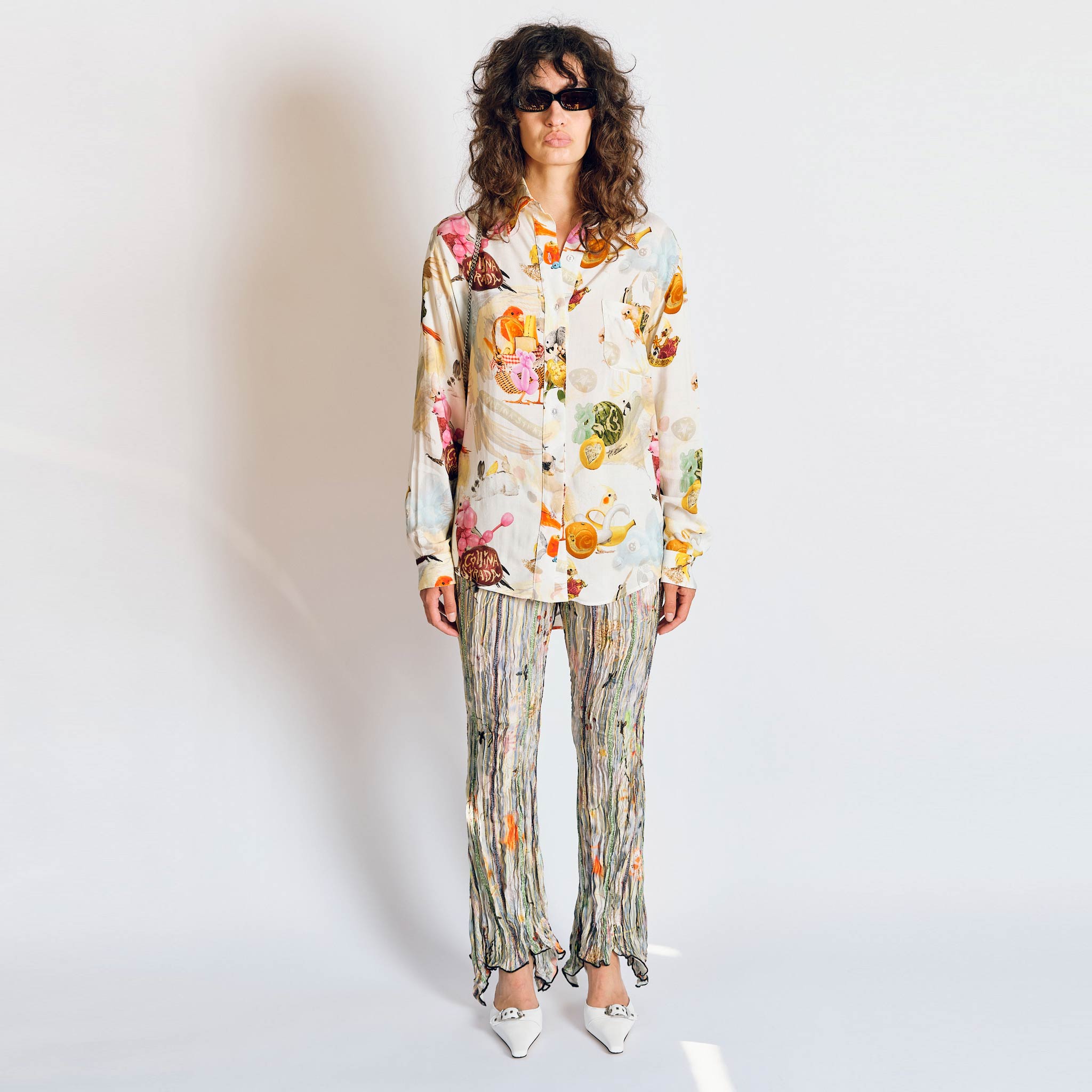 A model wears the pleated Dahlia trousers with light green, grey graphic floral print - full outfit view.