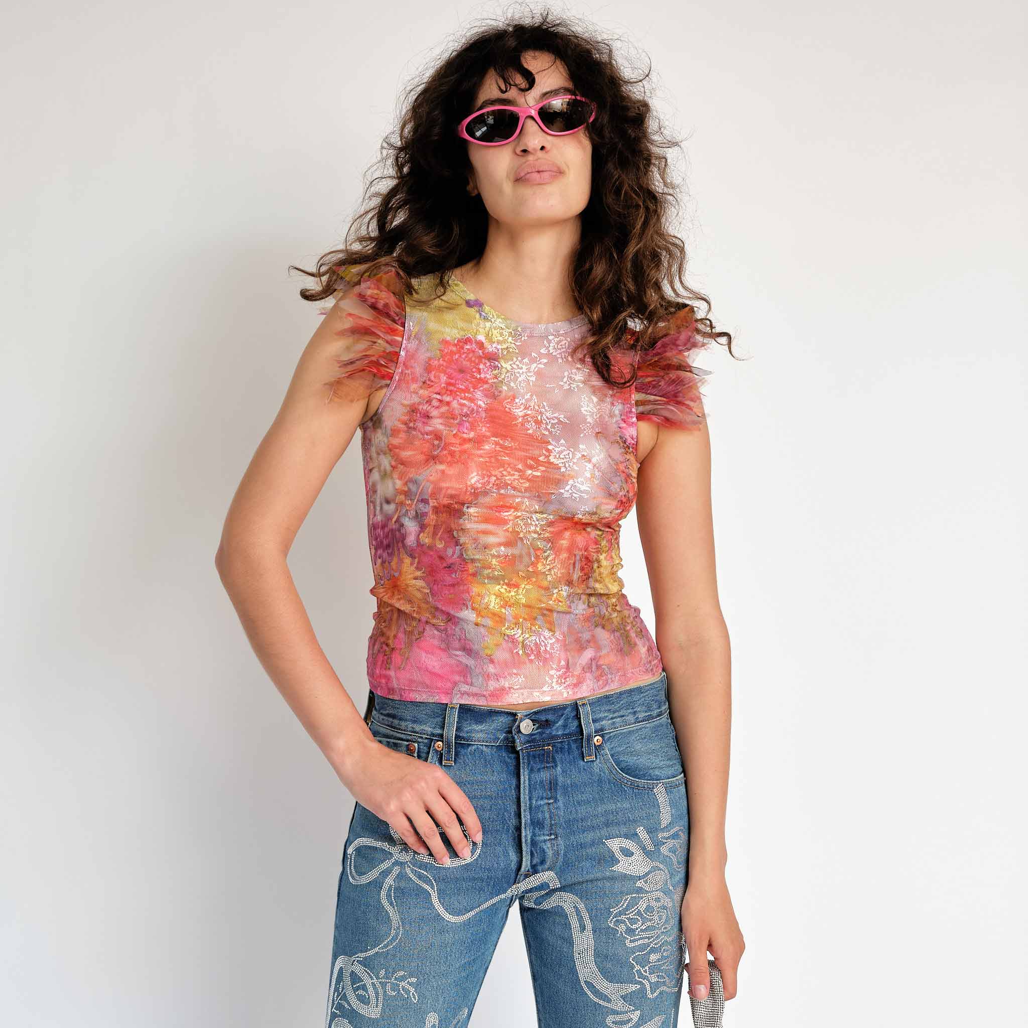 A model wears the Dachi top - a multicolored stretch lace tank top with pink feathers around the arm holes - front view.
