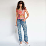 A model wears the Dachi top - a multicolored stretch lace tank top with pink feathers around the arm holes - full outfit view.
