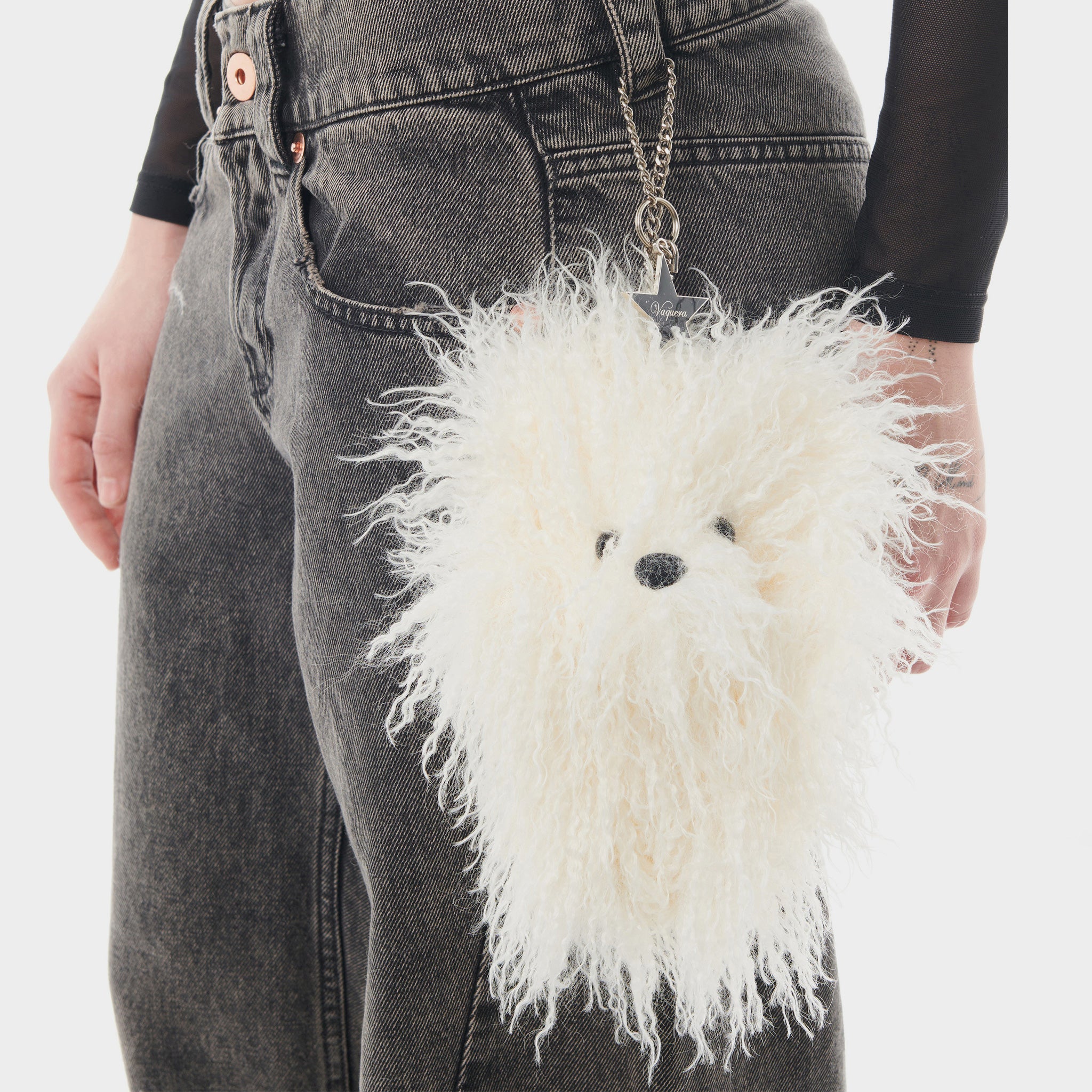 Side detail of model wearing the Furry Teddy Keychain - a large stuffed white teddy bear dangling off a silver keychain, attached to the belt loop of a model wearing black jeans.