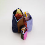 A set of 3 nylon travel pouches with different colored panels on each side of each bag, with the pouches zipped open to show examples of what can fit inside.
