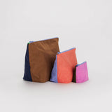 A set of 3 nylon travel pouches with different colored panels on each side of each bag, with the pouches standing up.