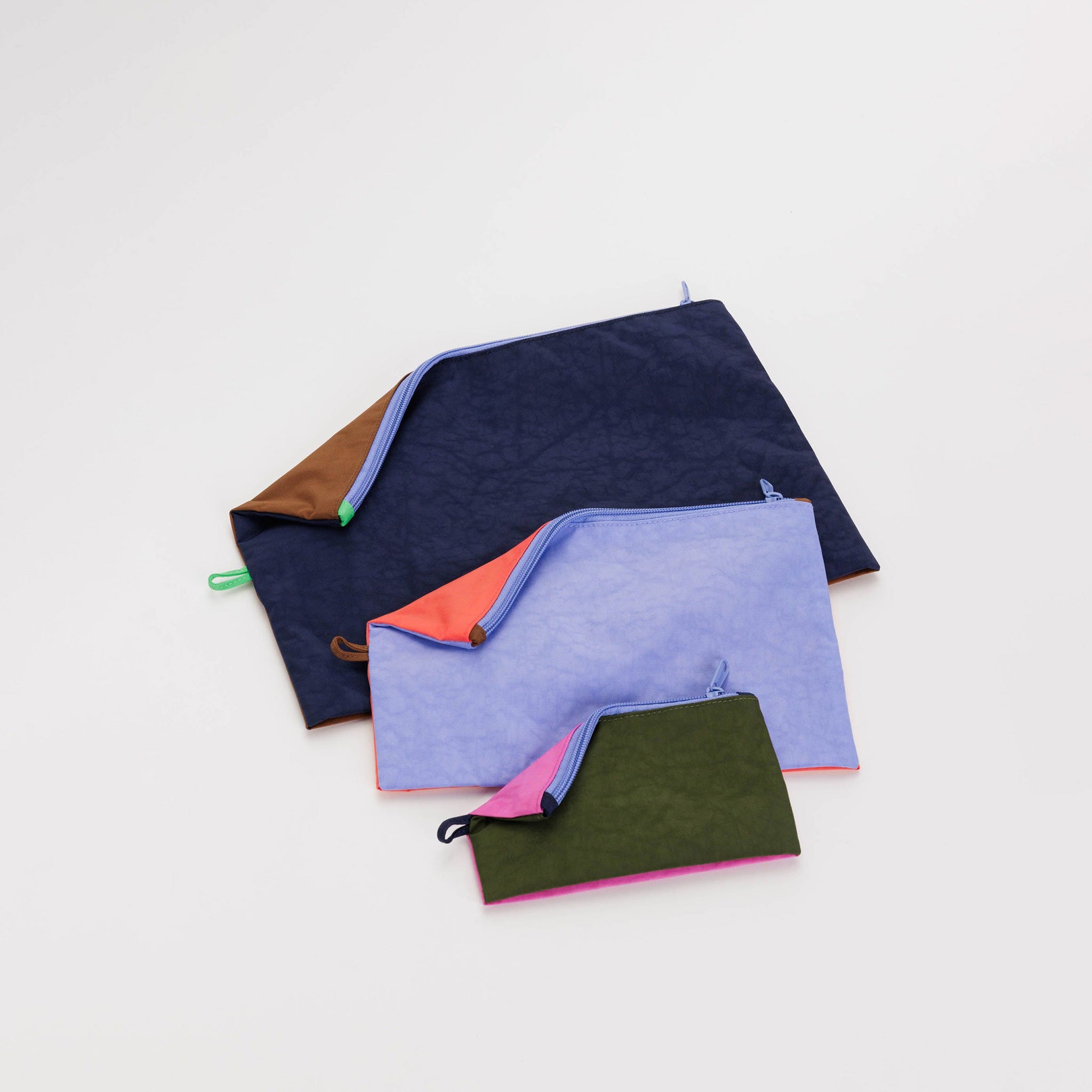 A set of 3 nylon travel pouches with different colored panels on each side of each bag, with the pouches laid flat.