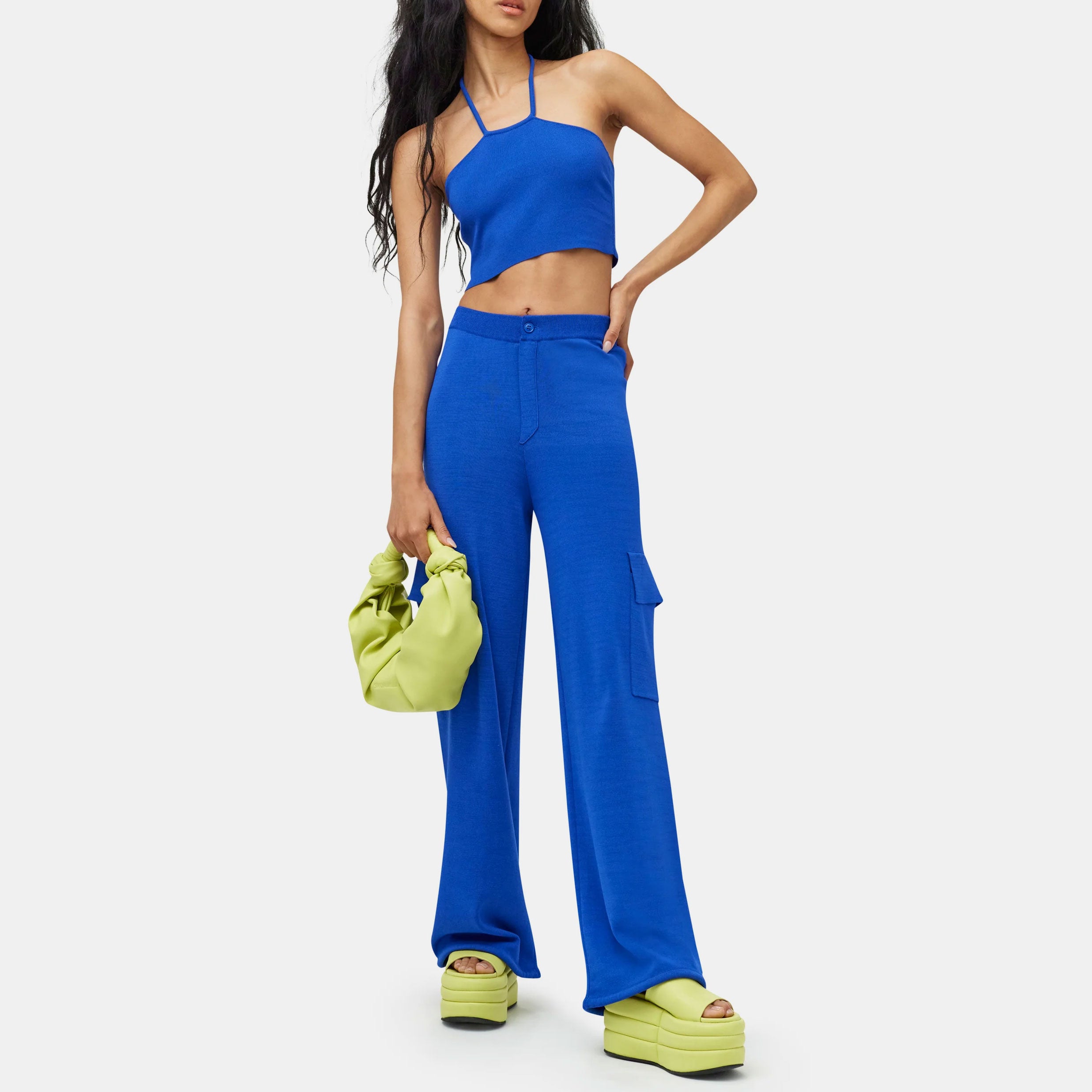 Close detail half body photo of the model wearing the Hesby Pant - a vibrant blue knit wide leg pant with side cargo-style pockets and a button & zip closure - full outfit view.