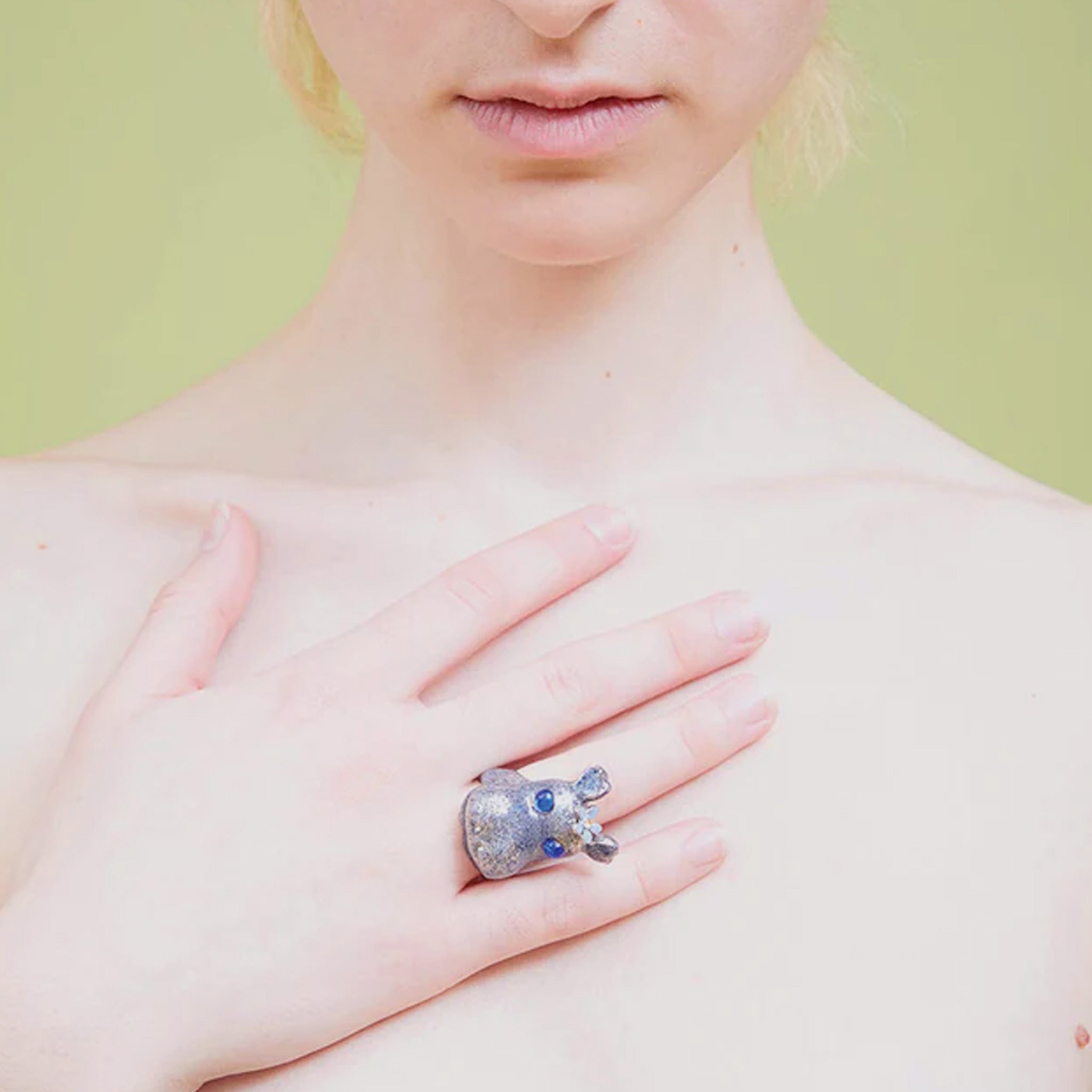 A model wears the Hippo Ring, a recycled pewter ring formed in the shape of a hippopotamus head, enameled in blue and white speckled paint with blue glass eyes.