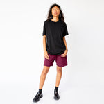 A model wears the Inside Out Tee in jet black, paired with merlot colored sweat shorts and black loafers - full outfit view.