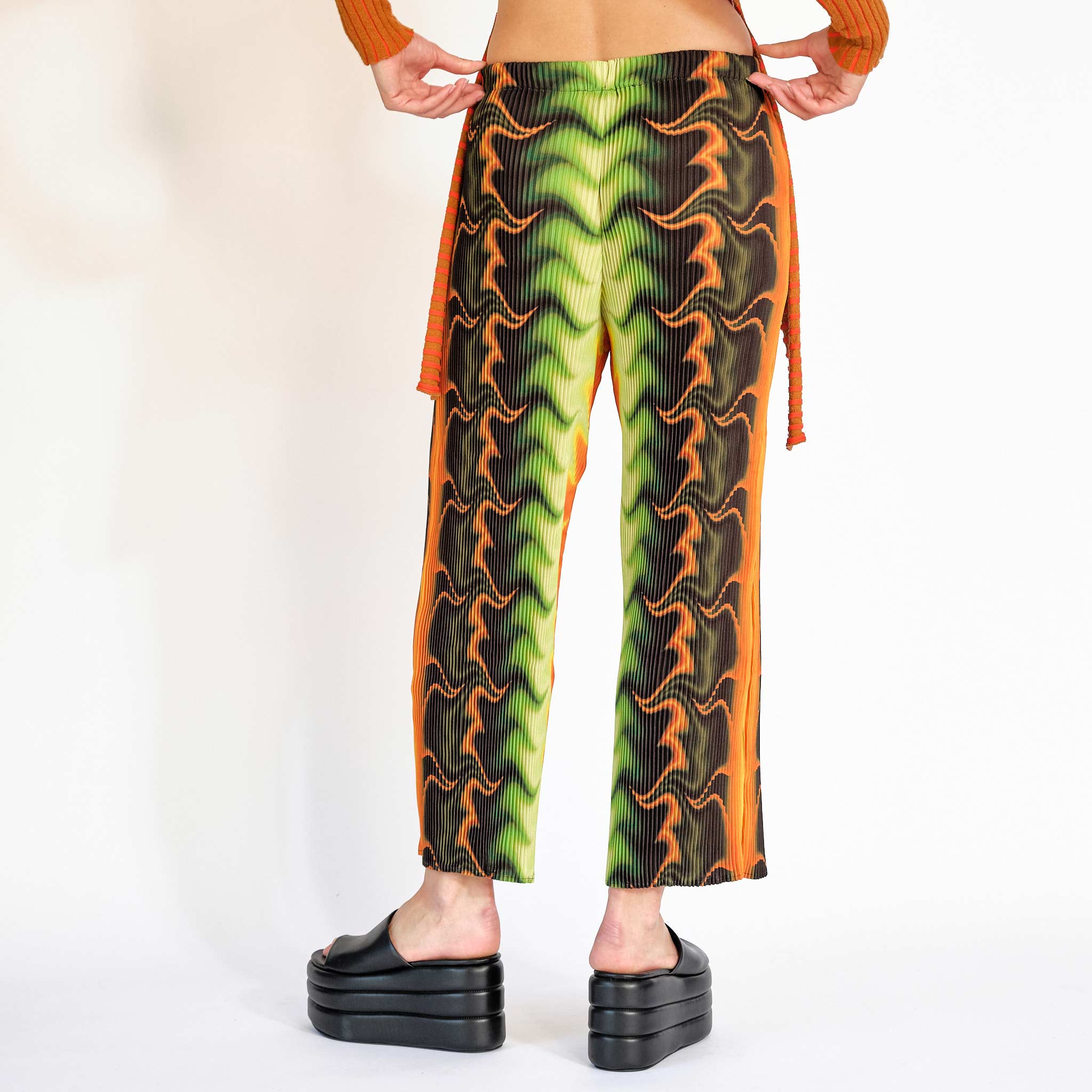 A model wears the green orange and black graphic printed pleated pant - back view.