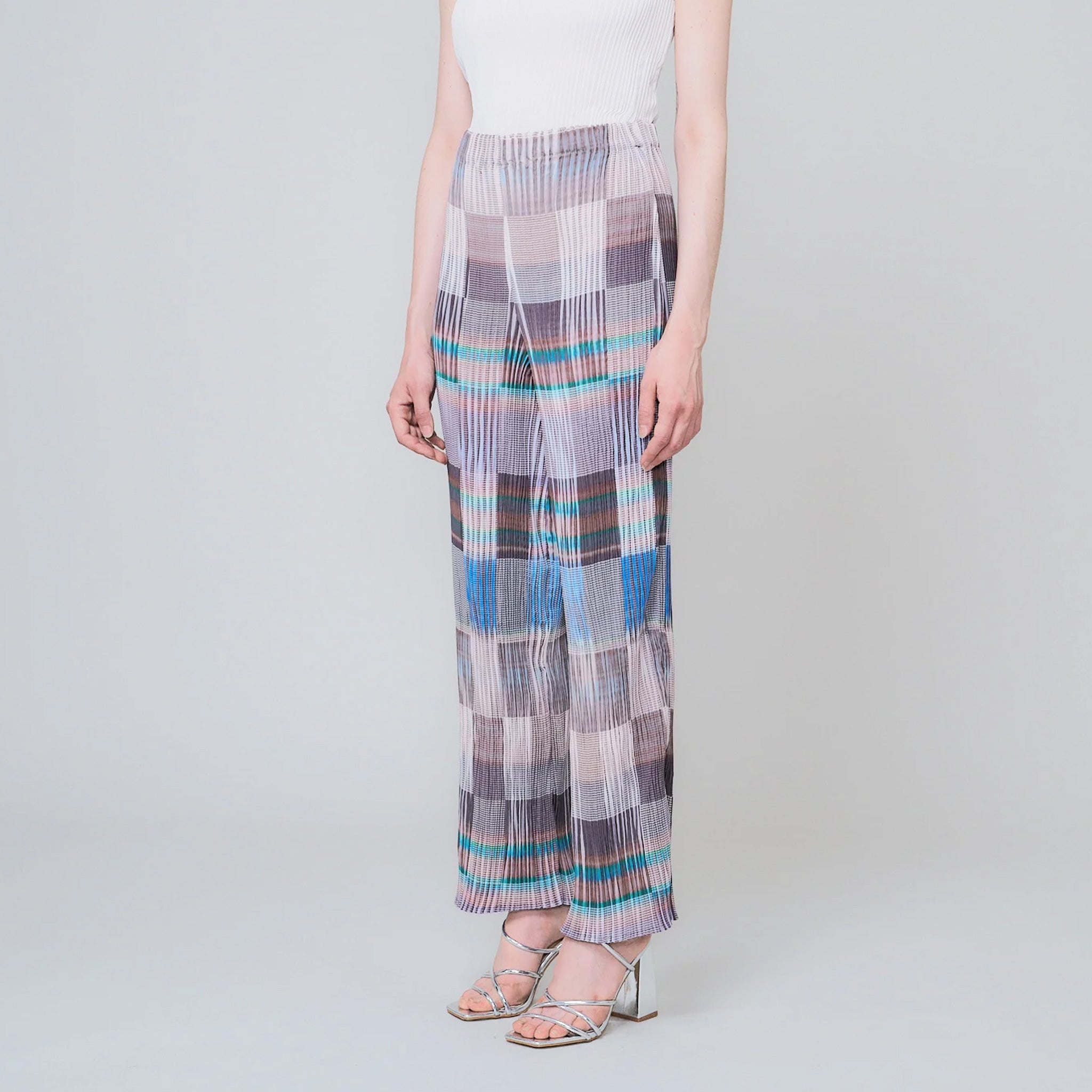 Pleated high waist trousers with a gridded graphic pattern in greys, whites, and blues - angled view on model.