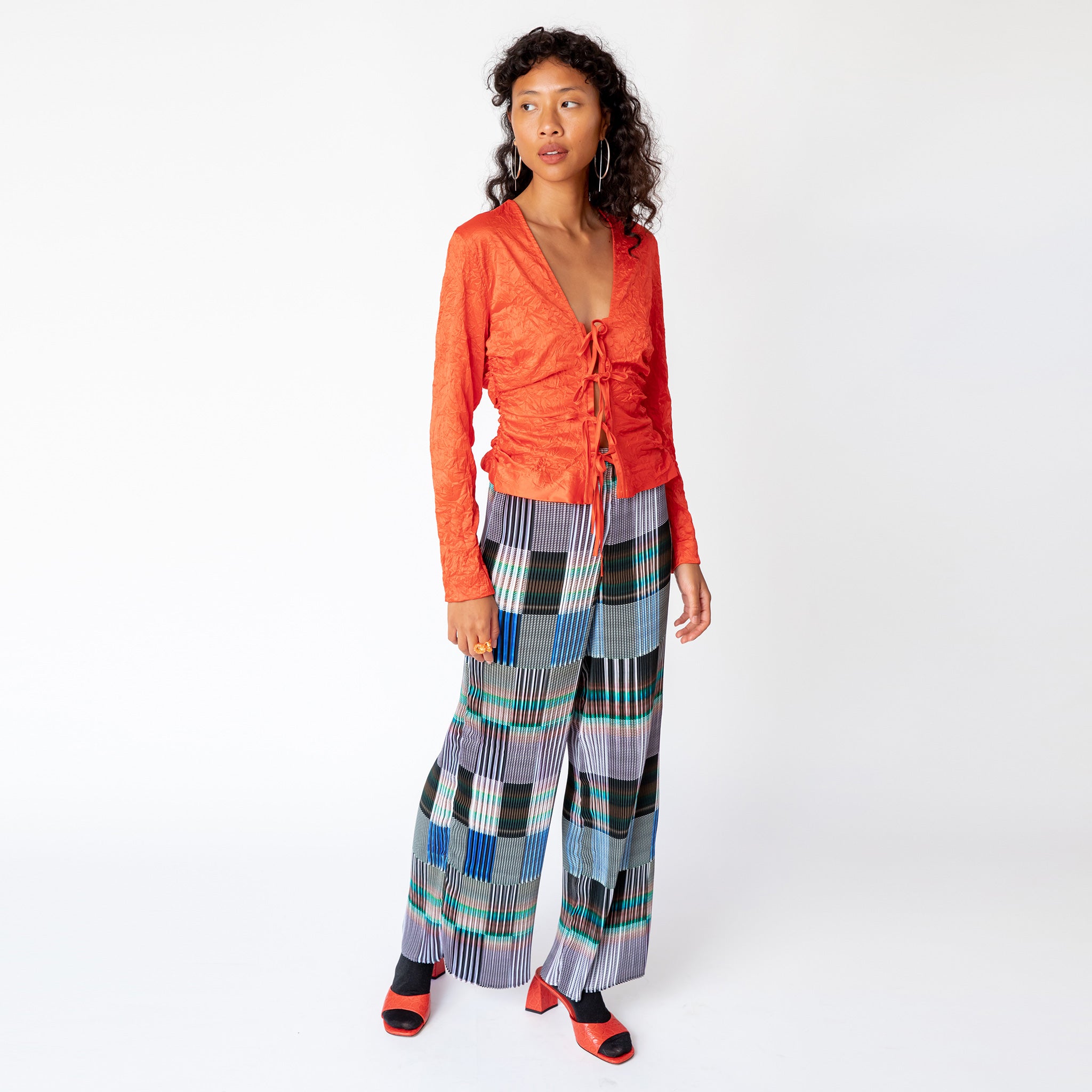Front view of the Julie Heuer pleated Jack Trousers in a gridded print pattern as worn with a vibrant red blouse.