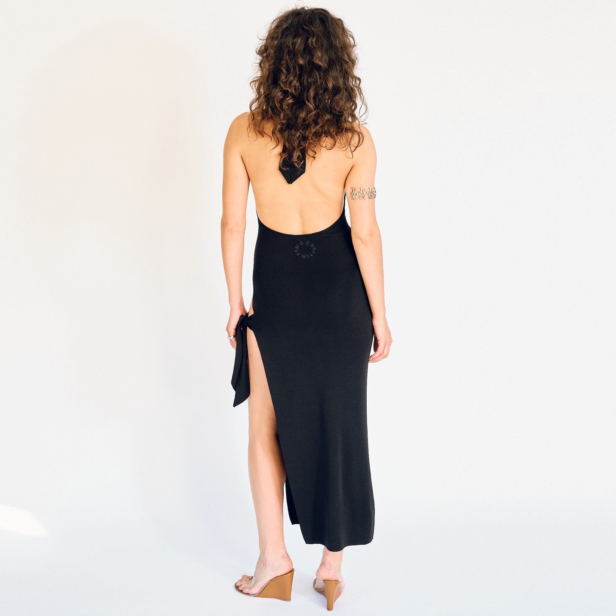 A model wears the Simon Miller Junjo tank style dress in black, with high side slits along the left leg - back view showing low back.