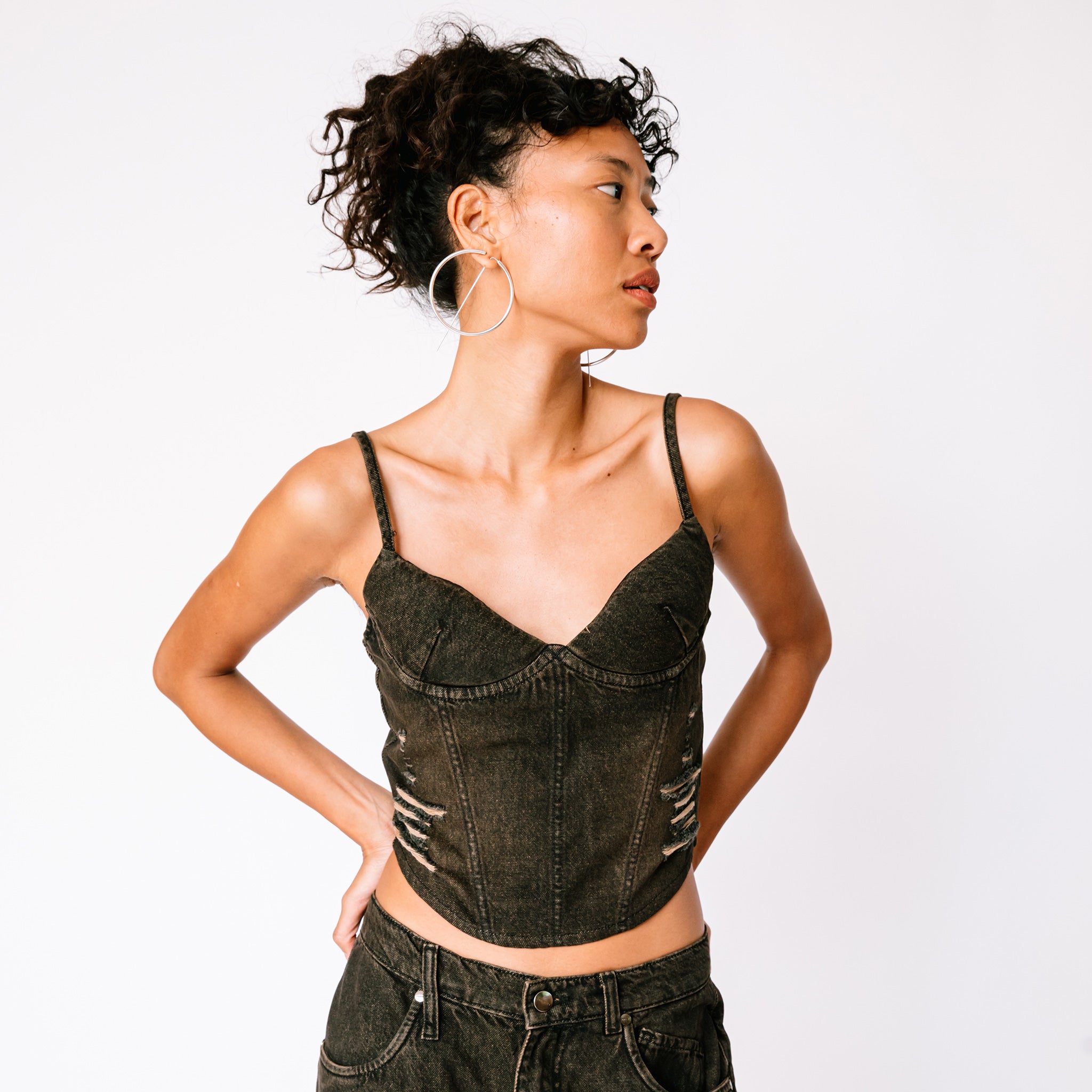 A model wears Miaou's faded black denim strappy Kiko corset paired with baggy jeans, front view.