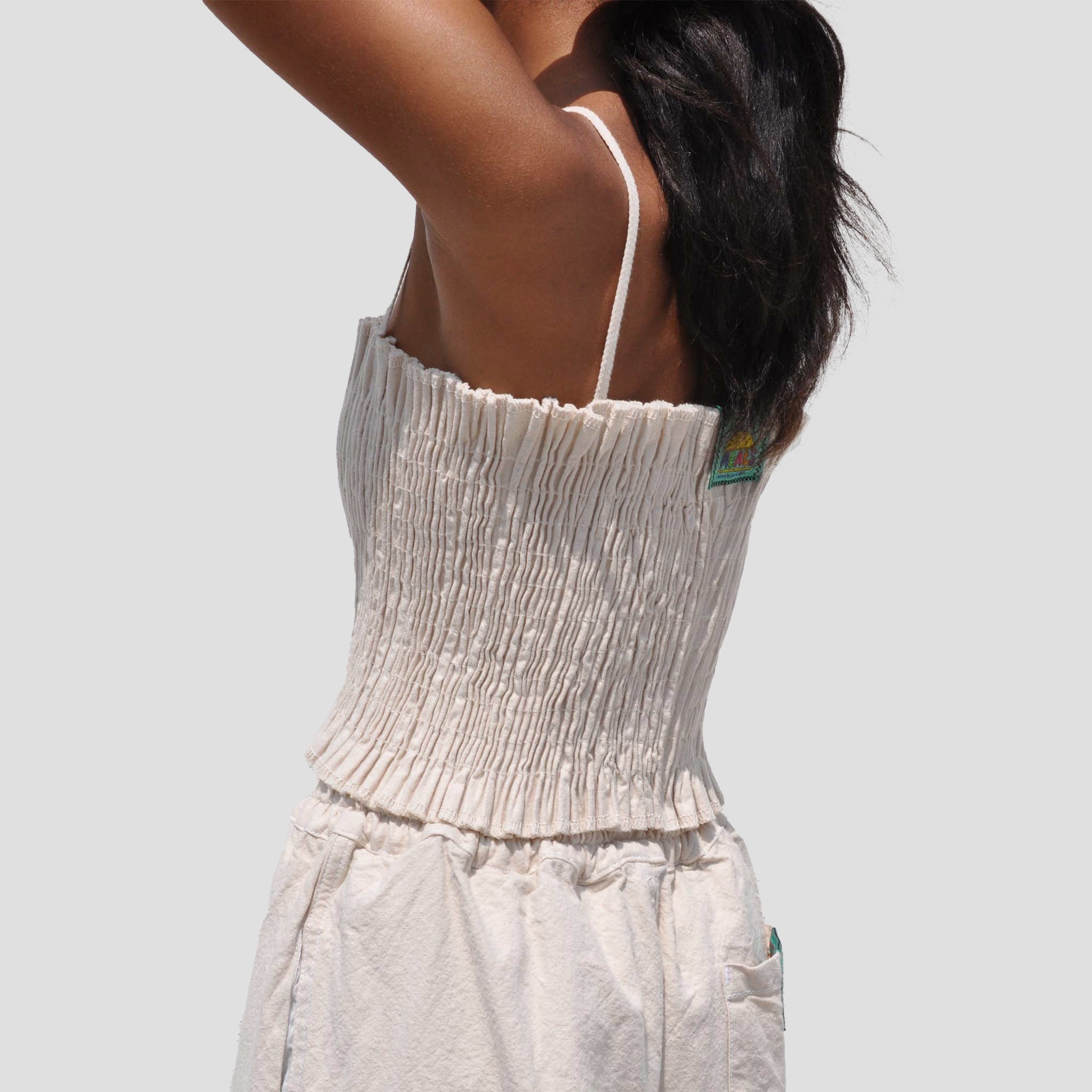 Photo of a model wearing the MEALS - Lettuce Stretch Top in flour (off white), a ruched top with shoulder straps - from the back.