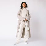 Side view of the Long Shawl Cardigan by Lauren Manoogian, with deep front pockets and wide sleeves, paired with white ribbed turtleneck and white pants.
