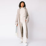 Side view of the Long Shawl Cardigan by Lauren Manoogian, with deep front pockets and wide sleeves, paired with white ribbed turtleneck and white pants.