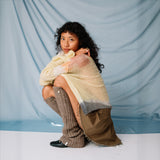 A model crouches down while wearing the light brown ribbed Luxy Leg Warmers by Sandy Liang.