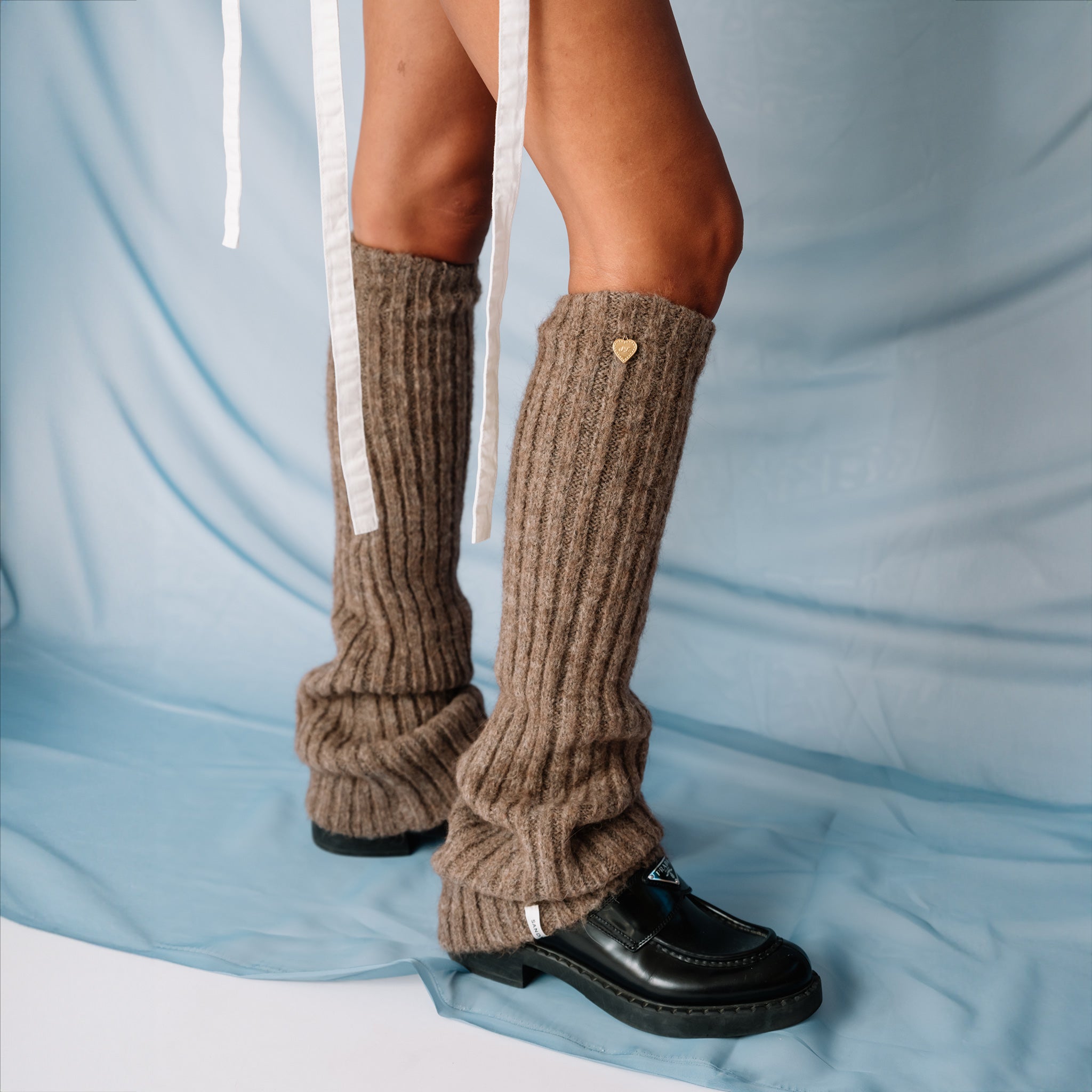 A close up of a model wearing the light brown ribbed Luxy Leg Warmers by Sandy Liang, paired with black loafers.