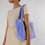 A periwinkle blue nylon shoulder tote with a puffy trapezoidal shape, on the shoulder of a model, close up.