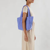 A periwinkle blue nylon shoulder tote with a puffy trapezoidal shape, on the shoulder of a model facing sideways.