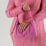 A pink nylon shoulder bag with a rectangular shape and top zipper, shown in the hands of a model.