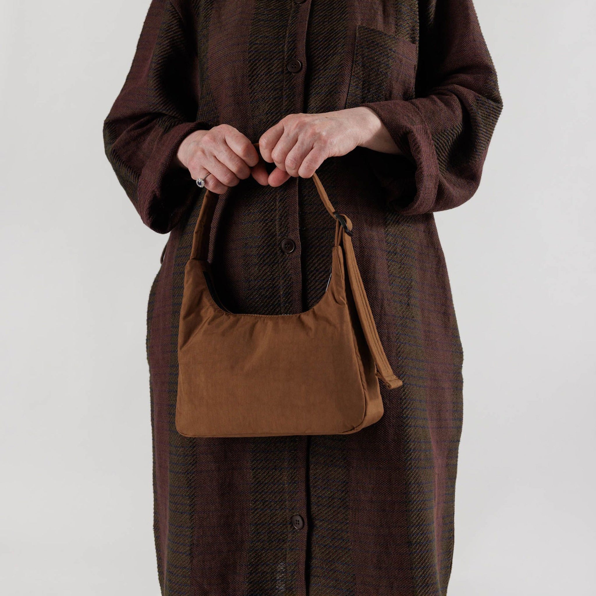 A brown nylon shoulder bag with a rectangular shape and top zipper, shown in the hands of a model.