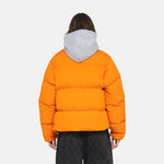 A model wears the Stussy Nylon Down Puffer jacket in orange over a grey hoodie - back view.