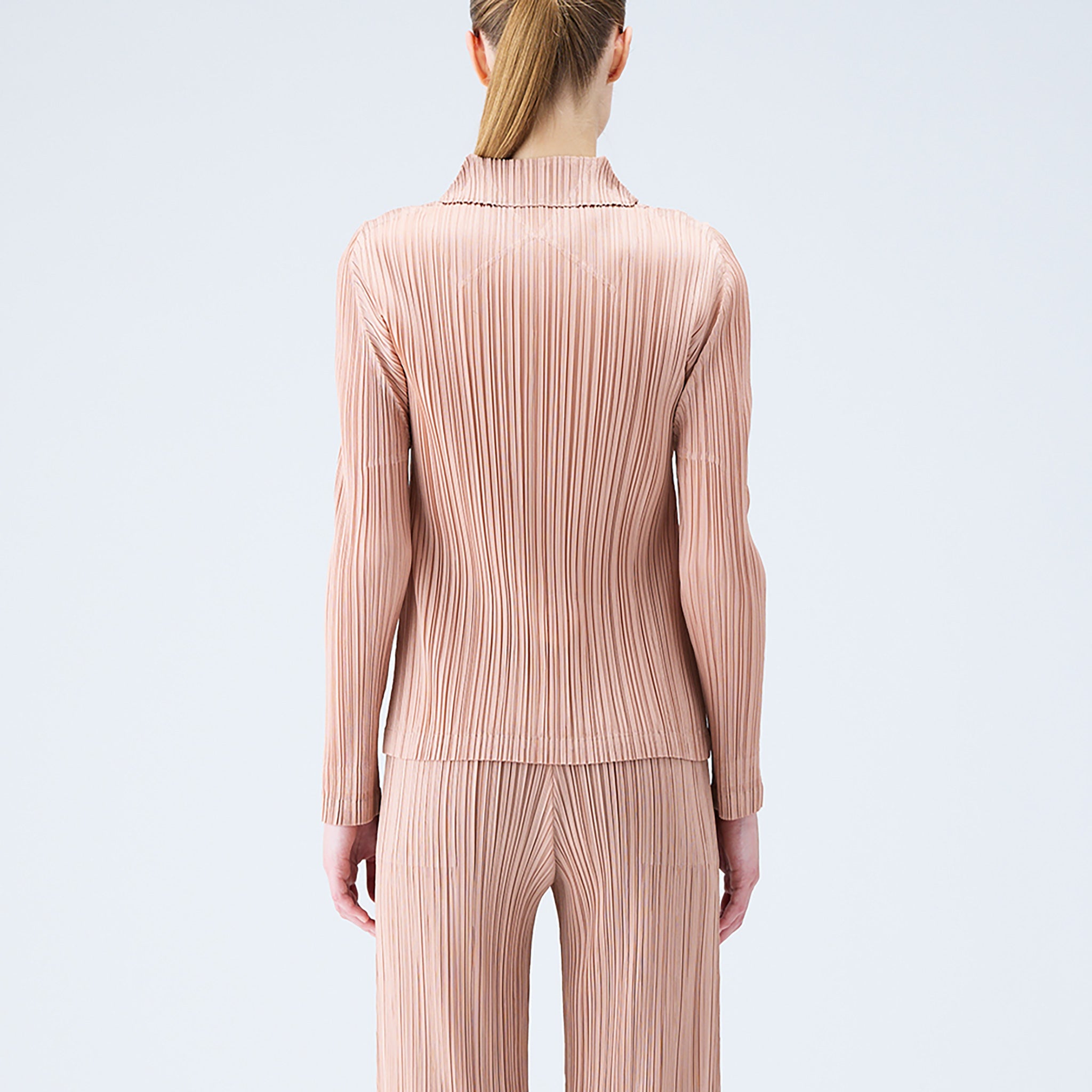 Back half body photo of model wearing the pleated polo top in the color beige. 