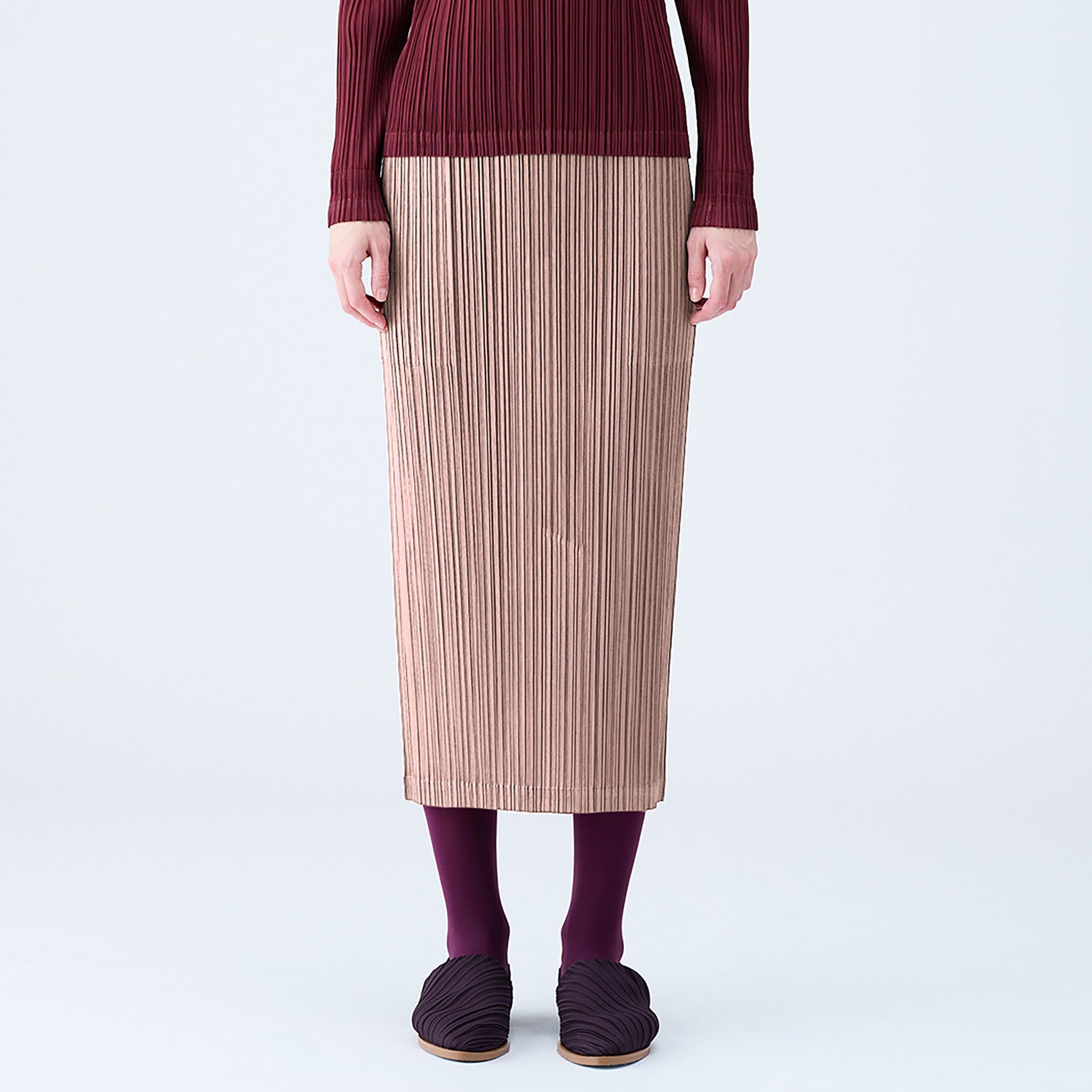 Close half body photo of model wearing a pleated midi skirt in the color beige. 