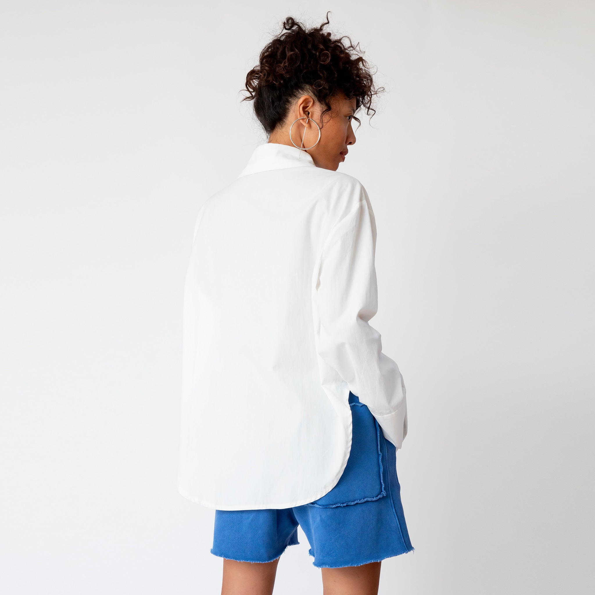 Back view of the Oversized Button Down Shirt in white paired blue sweat shorts.
