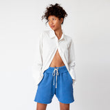 Front detailed view of the Oversized Button Down Shirt in white, worn half unbuttoned and paired with blue sweat shorts.