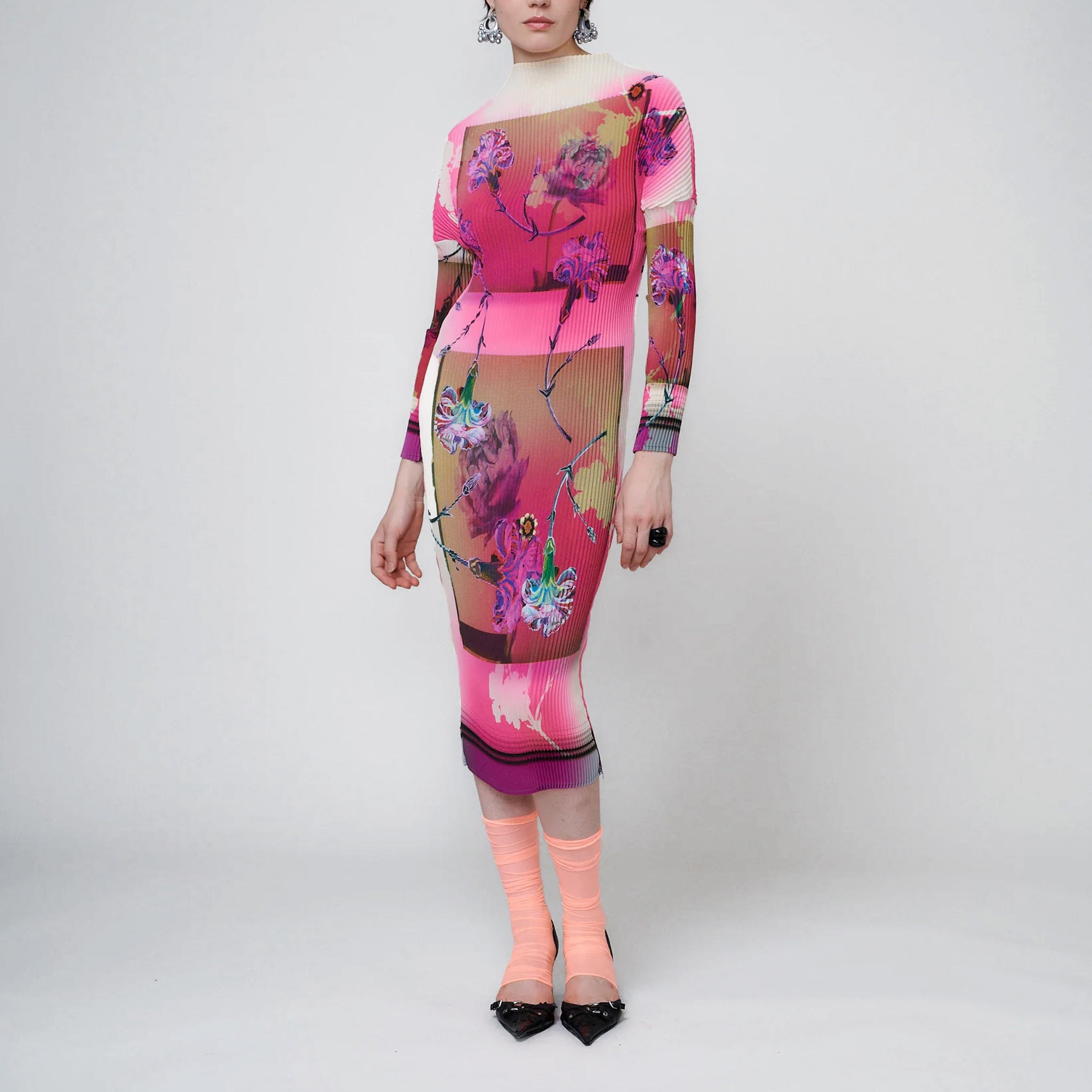 A model wears the midi-length pleated Pauki Dress in a vibrant pink and white floral print - front view.