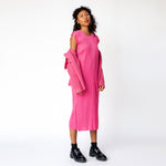 Full body photo of model wearing the pink pawn cardigan and a pleats long pink dress paired with black loafers.