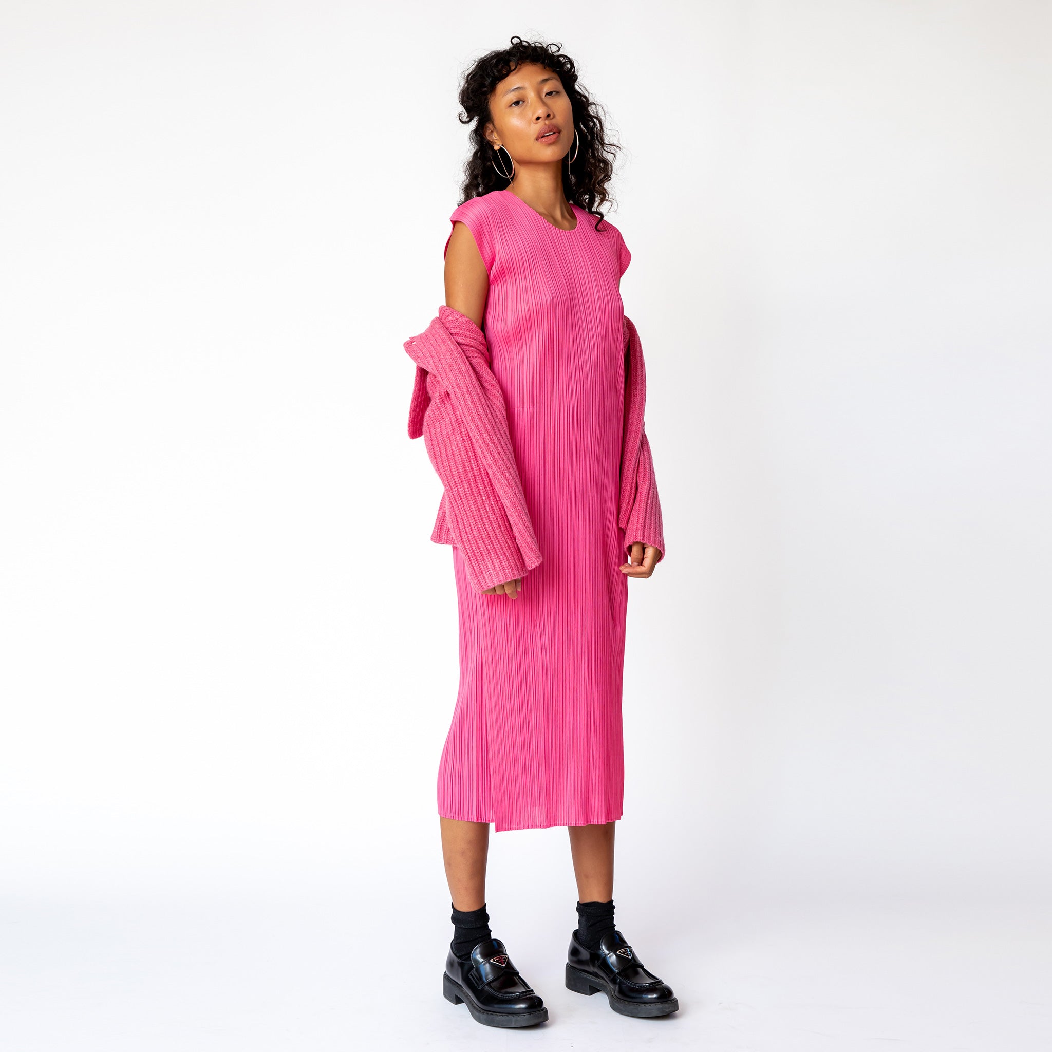 Full body photo of model wearing the pink pawn cardigan and a pleats long pink dress paired with black loafers.