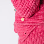 A model wears the chunky ribbed pink Paw Cardigan, detailed view of the heart shaped gold button.