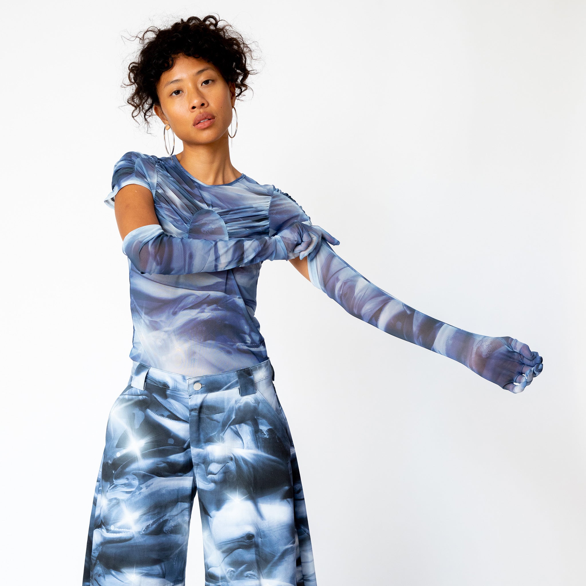 A model pulls up the sleeve on the blue and white dolphin printed semi-sheer opera gloves by Collina Strada.