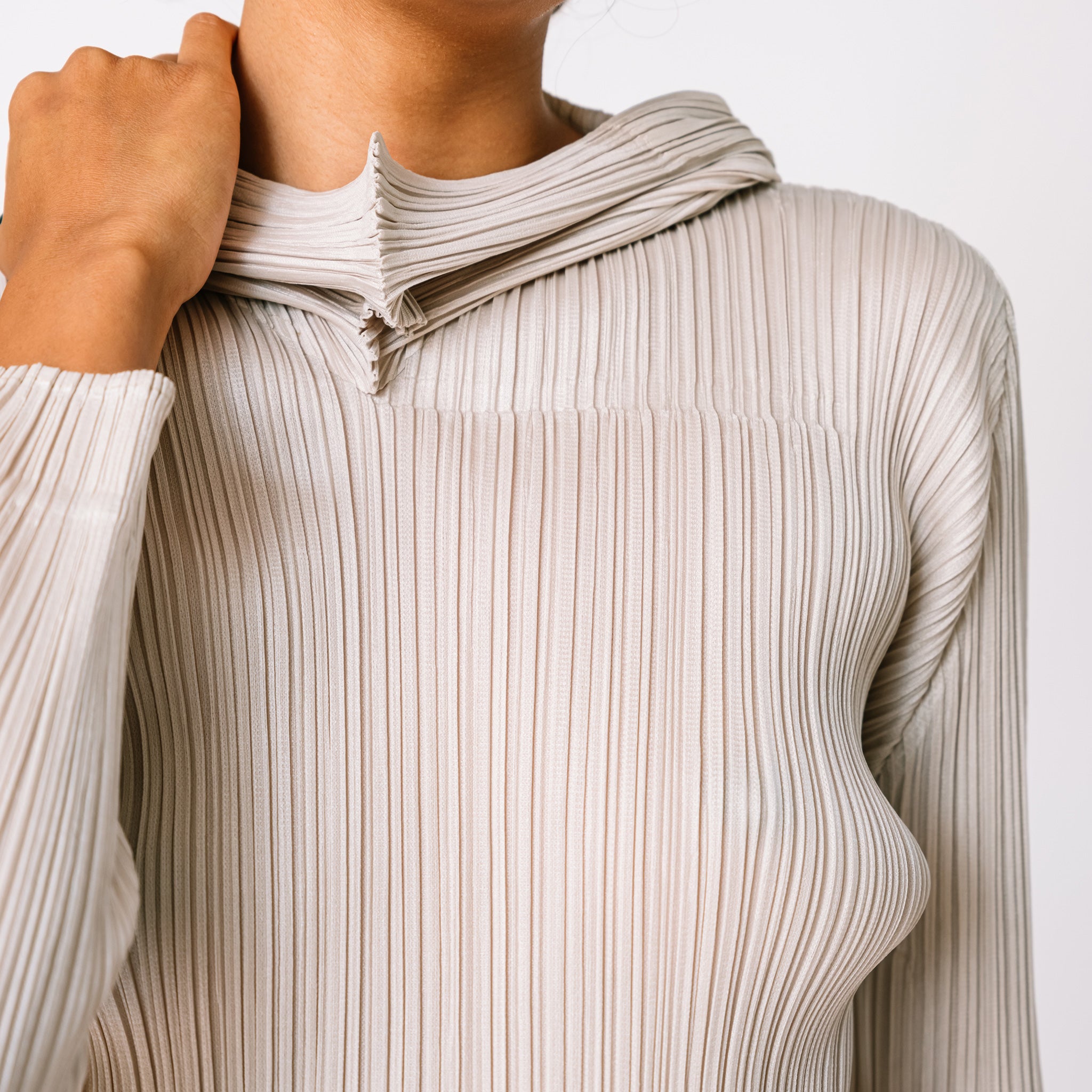 Detailed close up of the Pleats Please pleated hoodie in greige.