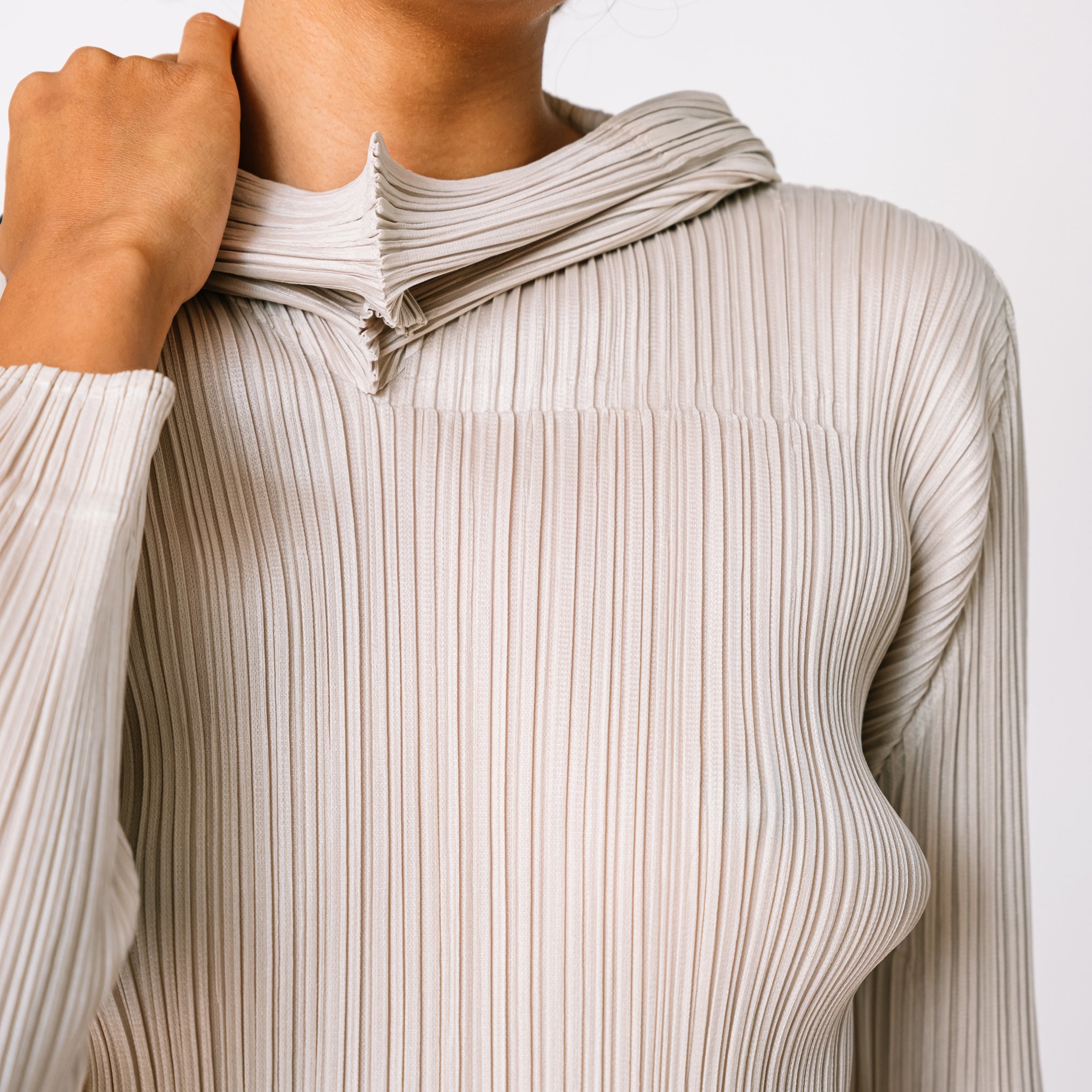 Detailed close up of the Pleats Please pleated hoodie in greige.